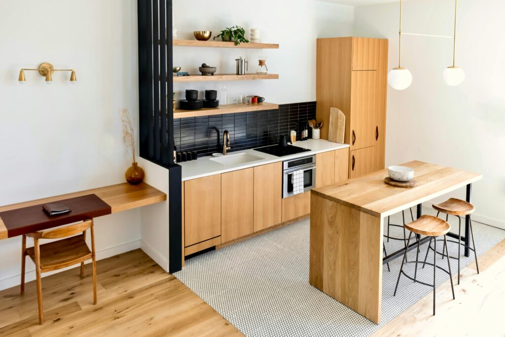 Best Furniture for Small Apartments | Space-Saving & Budget-Friendly Ideas (US & Canada) Light-filled modern kitchen interior with wooden furnishings and black accents.