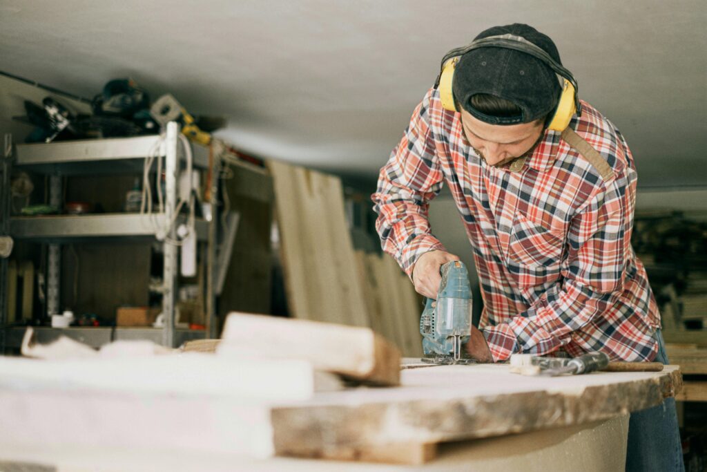 A skilled carpenter uses a power drill in a well-organized woodworking workshop.