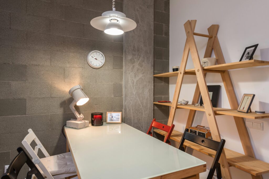 Comfortable colorful chairs with big white table near wooden unusual shelves in modern room